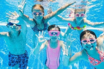 childrens swimming underwater in pool wearing goggles and smiling