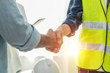 Construction professionals shaking hands at building site with hard hats and high visibility vest